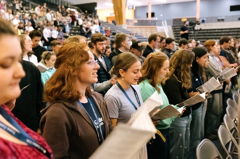 Jovens adultos se levantam para cantar durante o devocional comemorativo "100 anos de instituto" realizado na Arena da ICCU no campus da University of Idaho em Moscow, Idaho, no sábado, 26 de setembro de 2026.