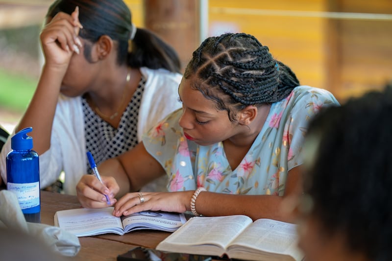 Uma jovem toma notas em um guia "For the Strength of Youth" com suas escrituras ao lado dela em uma mesa na República Dominicana em julho de 2025.