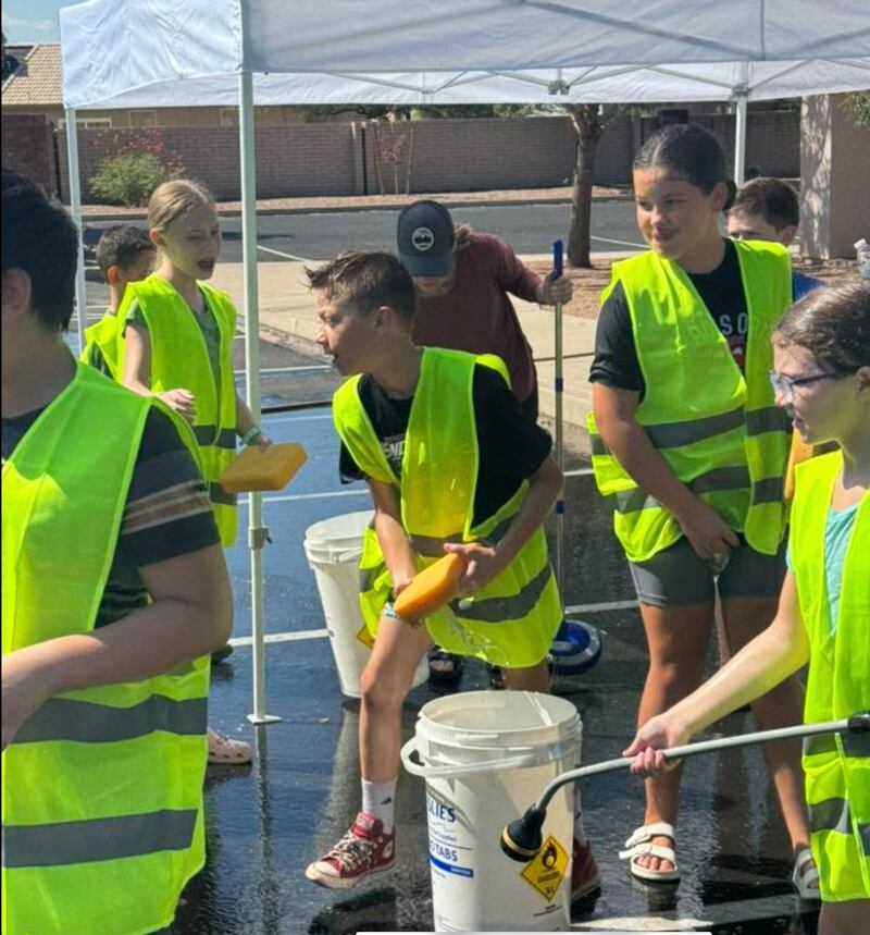 Crianças carregam suas esponjas e mangueiras para preparar-se para lavar um carro durante o lava-rápido gratuito e arrecadação de brinquedos, organizado pela organização primária da Estaca Peralta Trail Arizona, em Mesa, Arizona, em 11 de setembro de 2025.