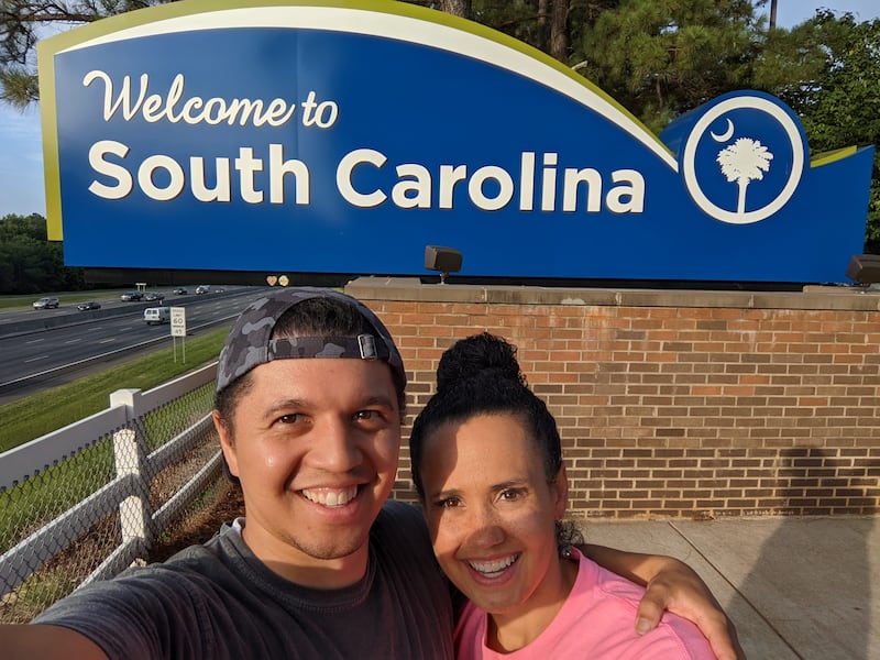 Vanessa Duerson e seu marido, Brian Kristofer Duerson, tiram uma selfie na frente da placa de boas-vindas de South Carolina no South Carolina Welcome Center em Fort Mill, South Carolina, em 30 de junho de 2022.