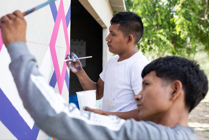 Keiber Epinayu, de costas, pinta símbolos antigos de Kanaas em infraestrutura de água com um jovem Wayúu em La Guajira, Colômbia em fevereiro de 2024.