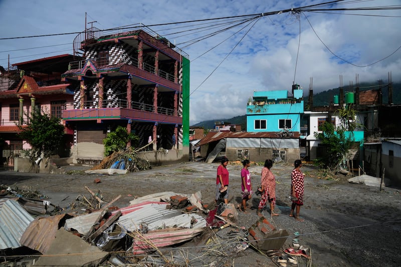Pessoas caminham diante dos danos causados por enchentes relâmpago em Devighat no distrito de Nuwakot no Nepal, quinta-feira, 27 de agosto de 2026.