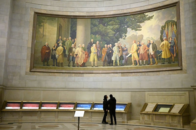 Dois visitantes observam exposições sob um grande mural que mostra a assinatura da Declaração de Independência nos Arquivos Nacionais na quinta-feira, 29 de janeiro de 2026, em Washington, D.C.