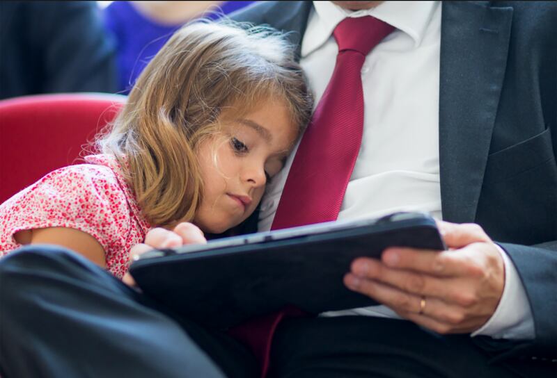 Uma filha se apoia no pai enquanto lê em um tablet.
