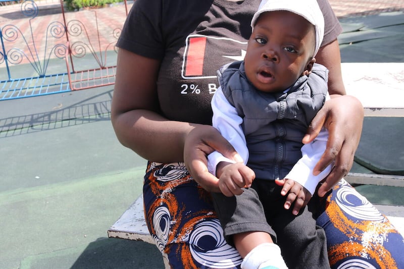 Samuel, com um ano de idade, sentado no colo de sua mãe fora do Lewanika General Hospital em Mongu, Zâmbia. Ele nasceu prematuro em dezembro de 2024.