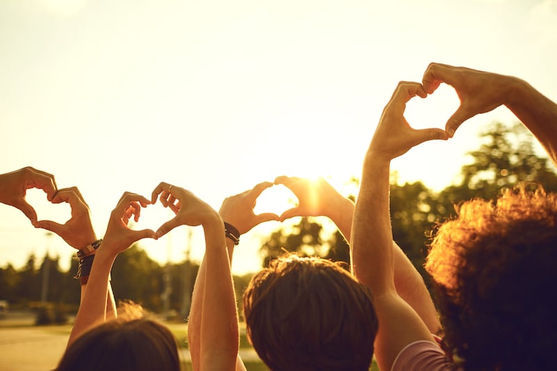 Mãos de um grupo de amigos em forma de coração contra o pôr do sol. Conceito de amor e amizade nas relações