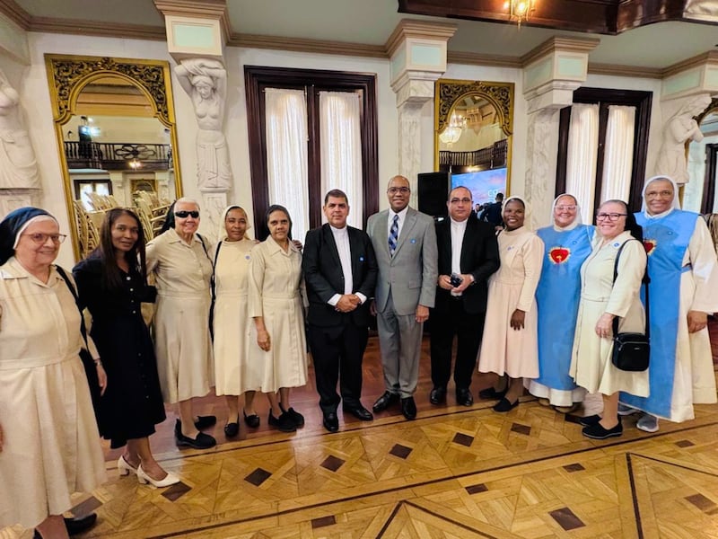 Élder Ahmad S. Corbitt, um Setenta Autoridade Geral e membro da presidência da Área do Caribe, está de pé em um terno cinza com outros líderes religiosos. Ele representou A Igreja de Jesus Cristo dos Santos dos Últimos Dias em um evento interconfessional de dia nacional de oração e ação de graças realizado em 7 de setembro de 2026, no Salão de Cariátides no Palácio Nacional em Santo Domingo, República Dominicana.