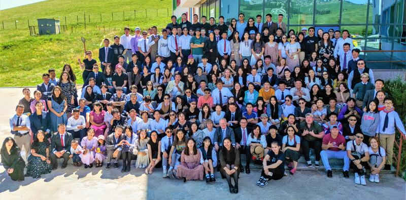 Participantes de uma conferência de jovens adultos solteiros no Japão posam para uma foto em agosto de 2023. Elder Jimo K. Esplin, Setenta Autoridade Geral, está sentado em um terno cinza com gravata azul na segunda fila, no centro. O Presidente Odgerel Ochirjav está sentado próximo ao meio, com uma camisa branca e chapéu.