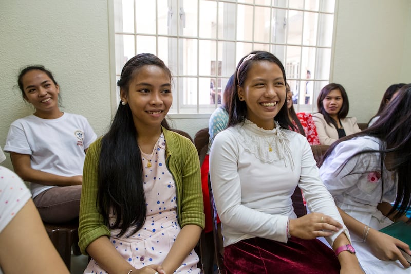 Jovens mulheres nas Filipinas sentam-se na aula juntas e sorriem.