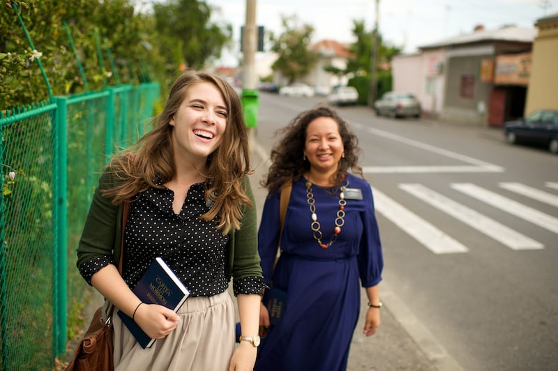 Duas missionárias na Romênia riem enquanto caminham juntas por uma rua.