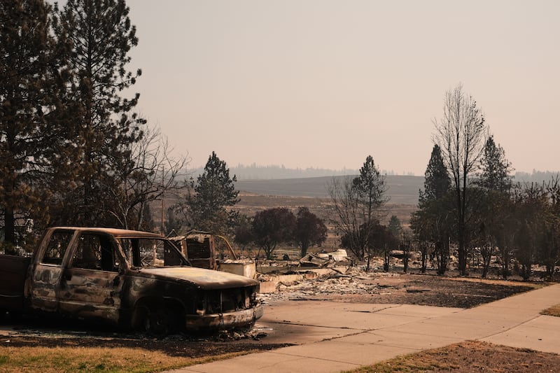 Um caminhão queimado fica em uma garagem perto de várias casas destruídas em um bairro residencial terça-feira, 4 de agosto de 2026, após um incêndio florestal atingir a parte norte de Spokane, Washington.
