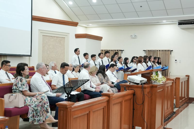 Elder Ulisses Soares do Quórum dos Doze Apóstolos e sua esposa, Sister Rosana Soares, à esquerda, ouvem enquanto um coro se apresenta durante um devocional para jovens adultos em Cebu em 16 de maio de 2026.
