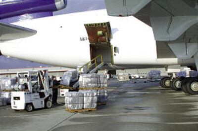 Fardos de cobertores embrulhados em plástico são carregados em correias transportadoras na pista no Aeroporto Internacional de Salt Lake. Cerca de 8.000 cobertores foram inclusos numa recente entrega humanitária.