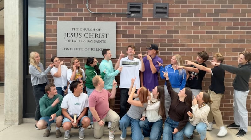Kaleb Jones, ao centro, aponta para o céu enquanto outros adultos jovens apontam para ele em um vídeo filmado no Utah Valley Institute of Religion em Orem, Utah, em 2026.