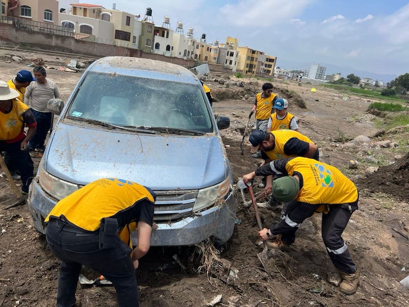 Voluntários de serviço de A Igreja de Jesus Cristo dos Santos dos Últimos Dias reúnem-se para remover a lama ao redor de um carro após as enchentes em Arequipa, Peru. Os deslizamentos de terra começaram após chuvas torrenciais em 19 de fevereiro de 2026.