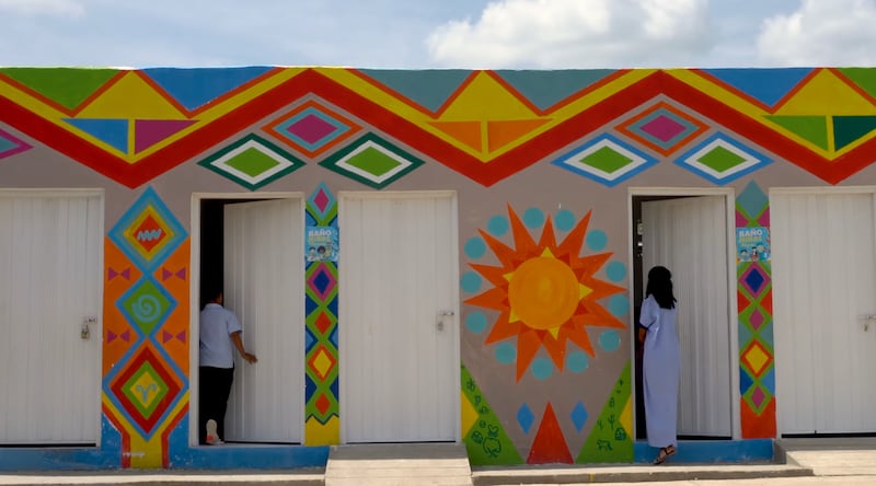 Dois jovens da comunidade Wayúu entram em um novo edifício com banheiros, torneiras e pias após serem pintados no estilo Kanaas em Guajira, Colômbia, em fevereiro de 2024.