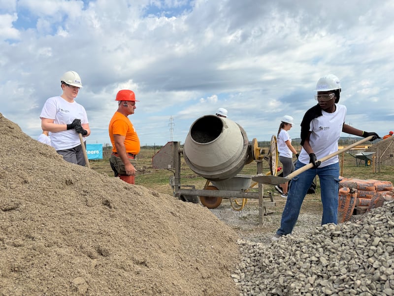 Adultos jovens preparam concreto sob a direção de um profissional de construção da Habitat para a Humanidade Romênia durante um projeto de serviço de uma semana em Berceni, Romênia, em agosto de 2026.