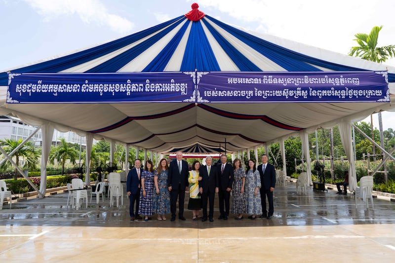 Élder Gerrit W. Gong e sua esposa, Irmã Susan Gong, no centro, unem-se a quatro Setenta Autoridade Geral e suas esposas sob uma tenda fornecida pelo governo cambojano no primeiro dia dos tours de casa aberta do Templo de Camboja em Phnom Penh na quarta-feira, 12 de agosto de 2026. A placa diz: "A unidade na religião traz paz e desenvolvimento. Parabéns pelo Templo de Camboja em Phnom Penh de A Igreja de Jesus Cristo dos Santos dos Últimos Dias."