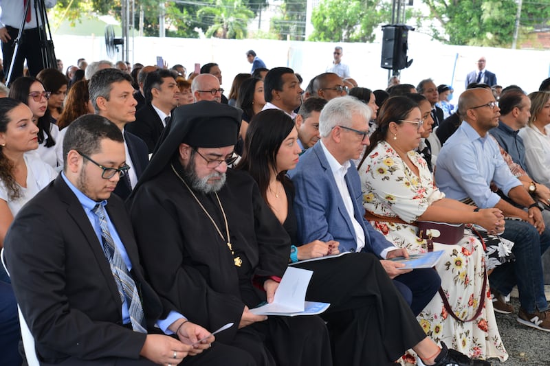 Uma grande congregação de pessoas sentadas em cadeiras ao ar livre usando suas melhores roupas de domingo.