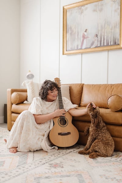 Angie Killian, compositora de "Anytime, Anywhere", posa para uma foto com seu violão e cachorro em sua casa em Salem, Utah, em 2024.