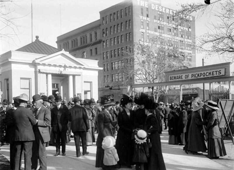 Multidões se reúnem para a conferência geral em abril de 1911. Observe a placa acima da entrada da Praça do Templo: “Cuidado com os batedores de carteira”. O antigo prédio do Deseret News é visto do outro lado da rua.