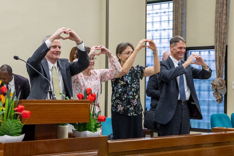 Elder David A. Bednar, Sister Susan Bednar, Sister Lynette Cook e Elder Carl B. Cook fazem sinais de coração com as mãos em direção aos jovens adultos solteiros em Kinshasa, República Democrática do Congo, sábado, 14 de março de 2026.