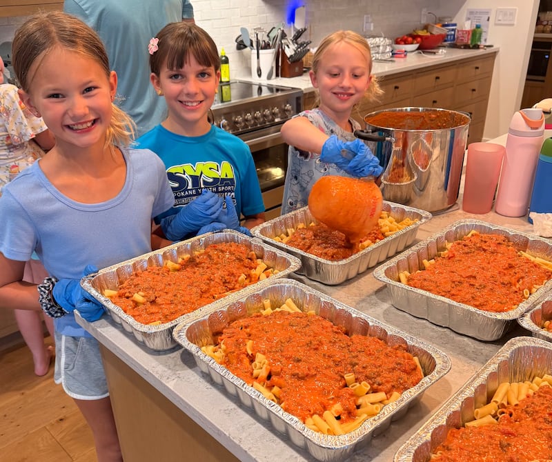Da esquerda para a direita, Sadie Coons, Adeline King e Hannah Shafer ajudam seu grupo de atividades das meninas da ala a prepararem refeições para levar às famílias desabrigadas pelos incêndios florestais em Spokane, Washington, em agosto de 2026.
