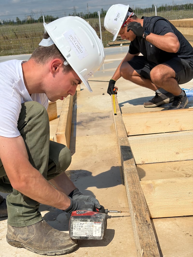 Adultos jovens medem e montam estruturas de parede de madeira para casas em construção em um projeto de serviço da Habitat for Humanity Romania em Berceni, Romênia, em agosto de 2026.