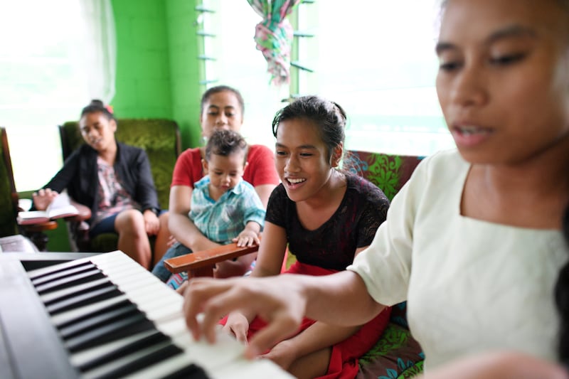 Uma família canta em casa enquanto uma filha toca no teclado.