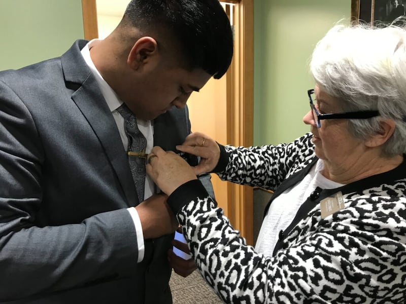 Síster Tina Dil, companheira do presidente Lindsay Dil do CTM da Nova Zelândia, ajuda um élder a colocar seu crachá de missionário pela primeira vez ao chegar ao Centro de Treinamento Missionário da Nova Zelândia em Auckland, Nova Zelândia, em 30 de junho de 2021.
