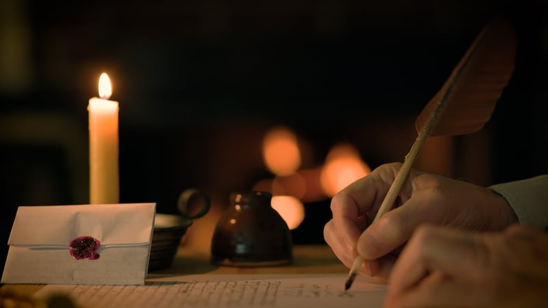 Um homem escreve uma carta usando uma pena, com uma lareira ao fundo.