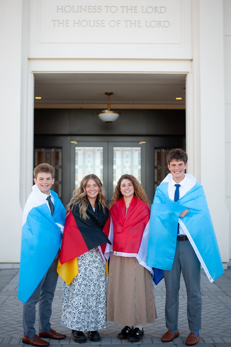 Isaac, Elle, Isabel e Eli Reid posam para uma foto com bandeiras representando onde servirão missões drapejadas em seus ombros.