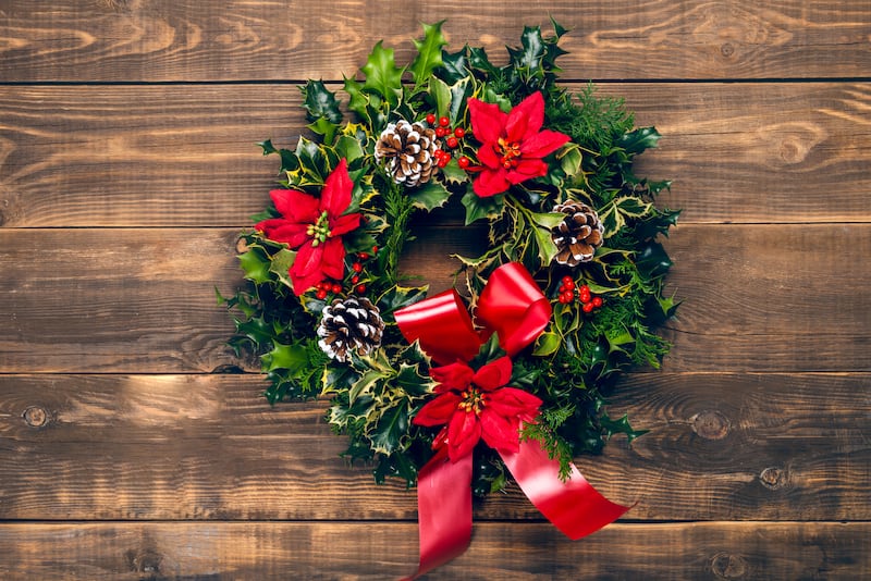 Guirlanda de natal com ramos perenes, folhas e pinhas com um laço vermelho em fundo de madeira.