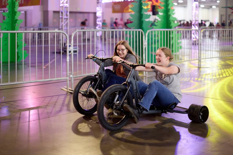 Duas mulheres participam de uma corrida de triciclo no Salt Palace Convention Center durante a Conferência de Adultos Solteiros da Área de Utah de 2026 em Salt Lake City, Utah, na sexta-feira, 14 de agosto de 2026.