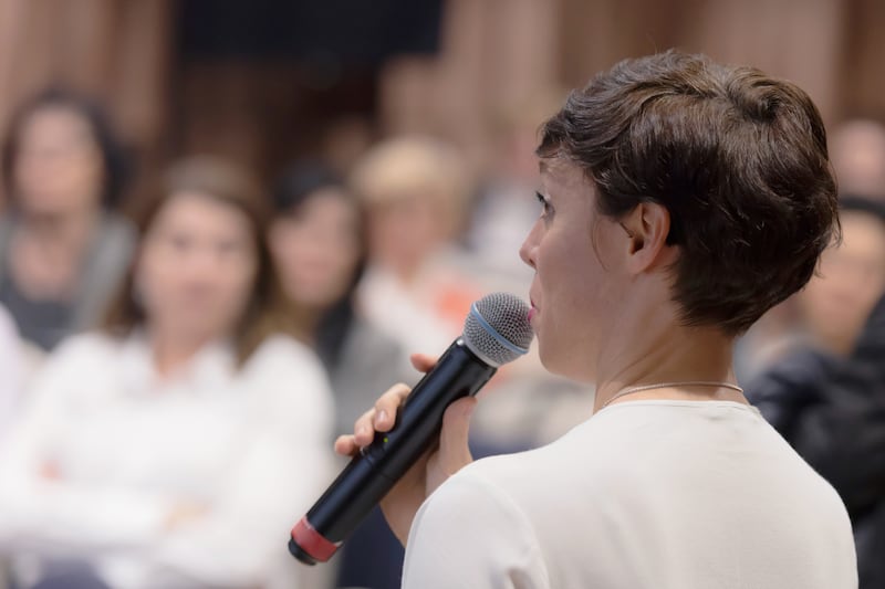 Uma mulher usa um microfone em uma aula.