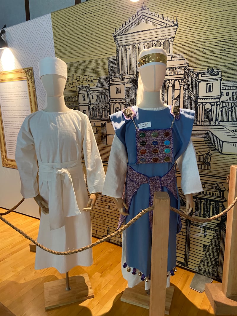 Um manequim vestindo um manto branco e um manequim vestindo um manto azul com 12 pedras coloridas na parte frontal no modelo do antigo tabernáculo móvel de Moisés.