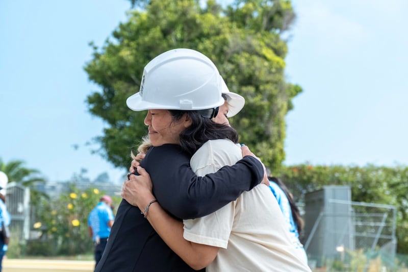 Voluntários abraçam-se durante um esforço do Habitat para a Humanidade para reconstruir casas destruídas durante o Incêndio Palisades durante um evento de quatro dias em setembro de 2026 em Los Angeles, Califórnia.