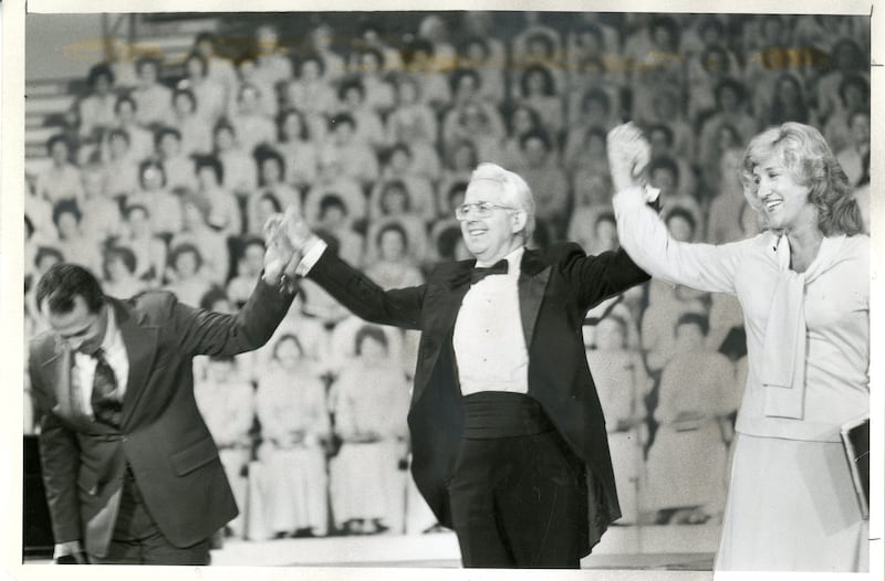 Lin de Paula, esquerda, Wany Santos Thrikill, direita, são membros do coral do Brasil. Jerold D. Ottley, diretor, os apresenta ao público durante os concertos do Coral do Tabernáculo na Praça do Templo em São Paulo, Brasil, em maio de 1981.