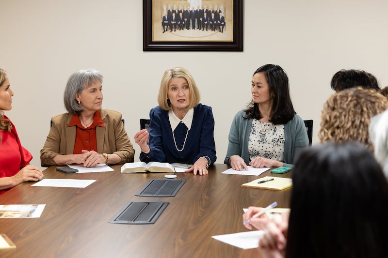 A Presidente Camille N. Johnson senta-se com suas conselheiras à cabeceira de uma mesa e fala aos membros do conselho geral consultivo da Sociedade de Socorro.