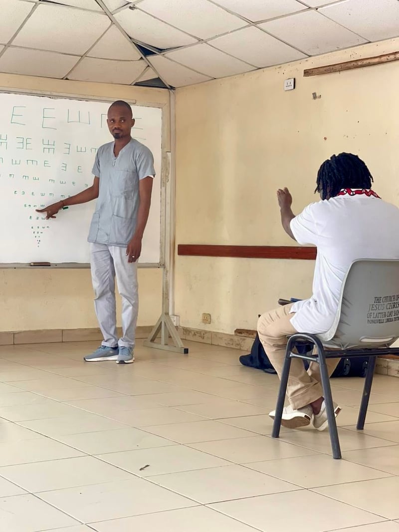 Adolphus Togbah, à esquerda, realiza um exame oftalmológico em uma clínica gratuita estabelecida em uma escola na Libéria.