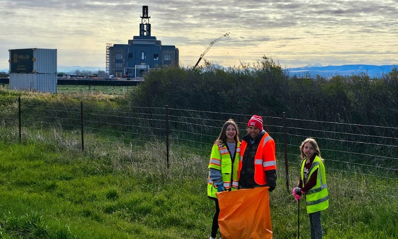 Jovens mulheres recolhem lixo ao longo da rodovia perto de Rexburg, Idaho, como parte do Dia Global de Serviço Jovem no sábado, 25 de abril de 2026. O Templo do Rio Teton Idaho está em construção ao fundo.