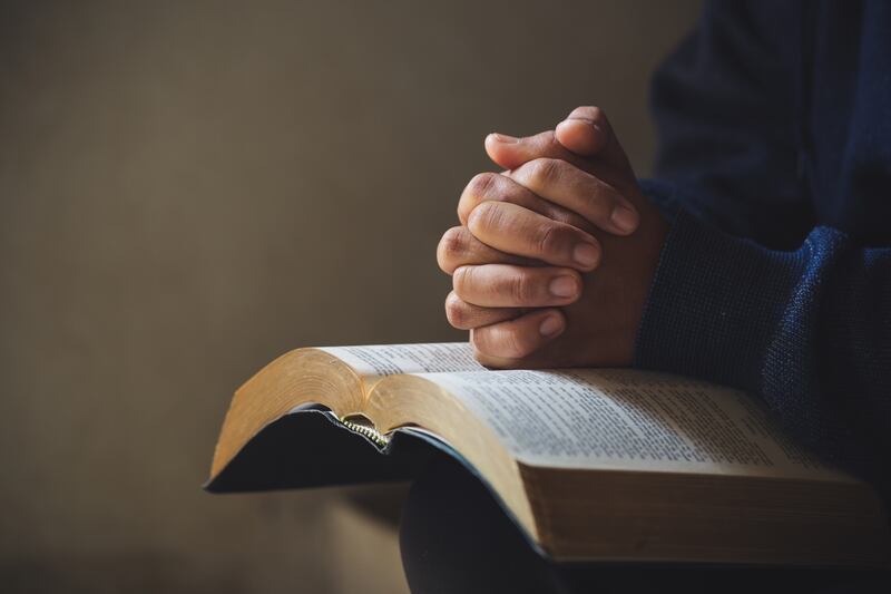 Mãos estão postas em oração sobre uma Bíblia Sagrada.
