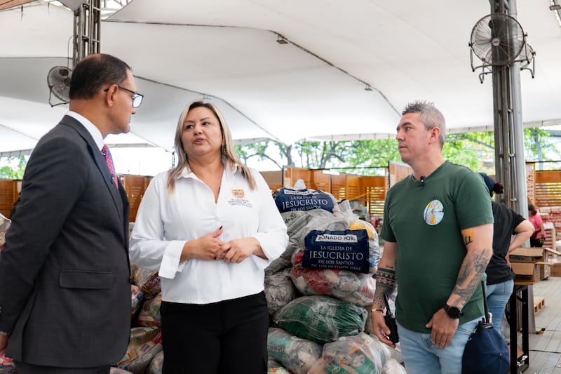 Élder Harold Truque, um Setenta da Área de Cali, Colômbia, à esquerda; conversa com Natalia Lasso, assessora do escritório do prefeito de Cali, ao centro; em um centro de coleta principal para distribuir 1.000 kits de alimentos para várias áreas afetadas por um terremoto em Cali, Colômbia, em agosto de 2026.