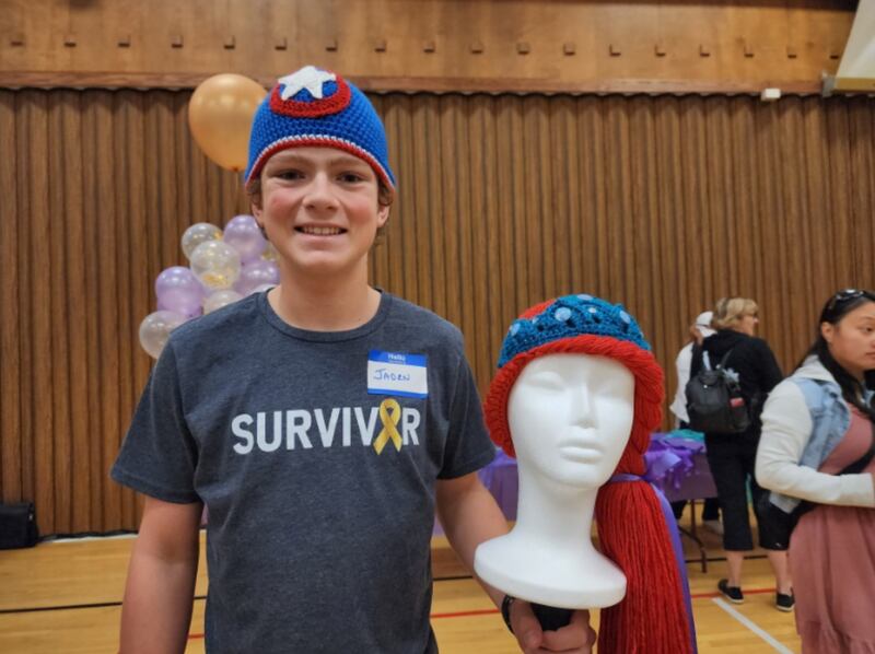 Jaden Wenger, um sobrevivente de câncer infantil, usa a peruca do Capitão América que ganhou, e mostra outra peruca feita por voluntários durante o Magic Yarn Project do ServirAgora na sede da Estaca Saratoga Califórnia, dia 21 de outubro de 2023.