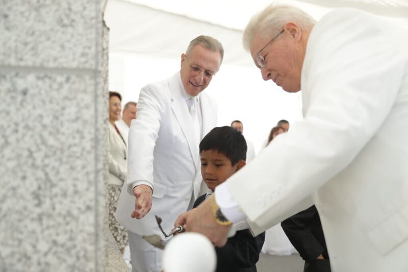 Élder Ulisses Soares, à esquerda, e bispo Dean M. Davies ajudam um garotinho a colocar argamassa na pedra angular do Templo de Arequipa Peru no dia 15 de dezembro, 2019.