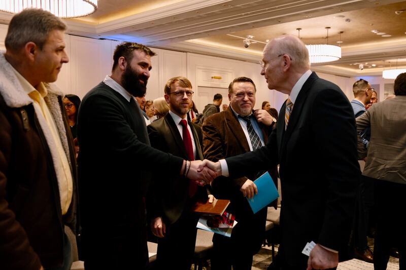 Elder Dale G. Renlund do Quórum dos Doze Apóstolos aperta as mãos com Alin Ardeleanu, um sacerdote ortodoxo, na conferência do distrito da Romênia Bucareste em 22 de fevereiro de 2026.