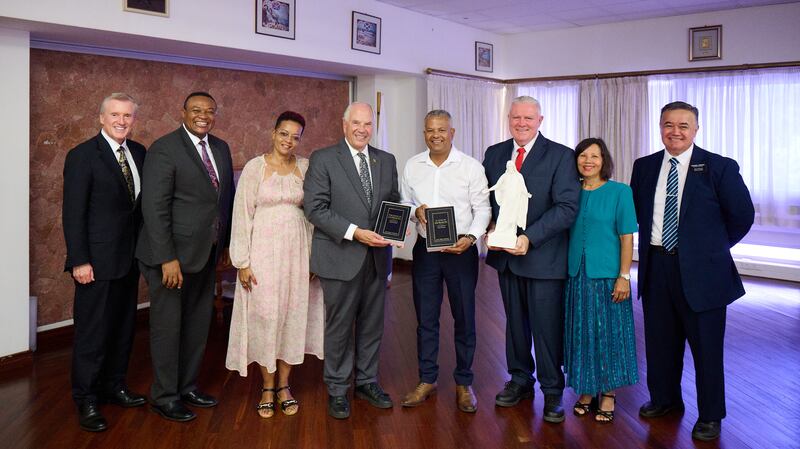 Elder Ronald A. Rasband está com Sebastien Pillay, o vice-presidente de Seychelles, enquanto seguram duas cópias do Livro de Mórmon, em Victoria, Seychelles, 29 de outubro de 2025. Também estão na foto Elder Kevin R. Duncan, Elder Thierry K. Mutombo, Deborah Maimee, Elder Evan Healy e Sister Marie Healy, e o Presidente da Missão Quênia Nairobi Leste, David T. Onekawa.