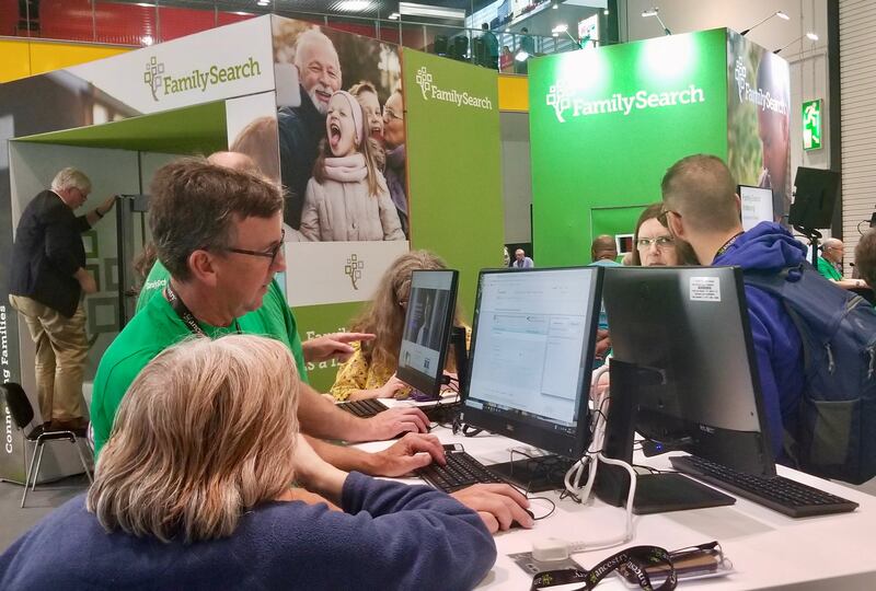Participantes conferem com equipe na mesa do FamilySearch na RootsTech Londres na área de exibição do centro de convenções London ExCel na quinta, dia 24 de outubro, 2019.
