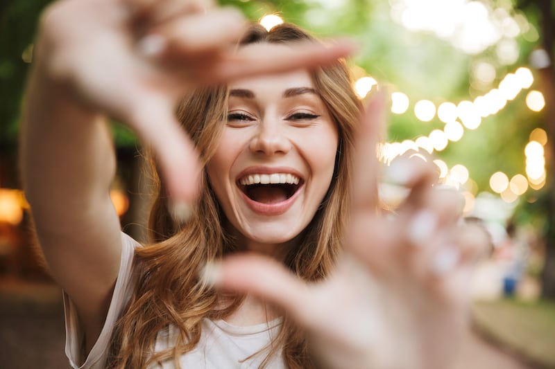 Close up of happy young girl showing frame with fingers while standing at the park