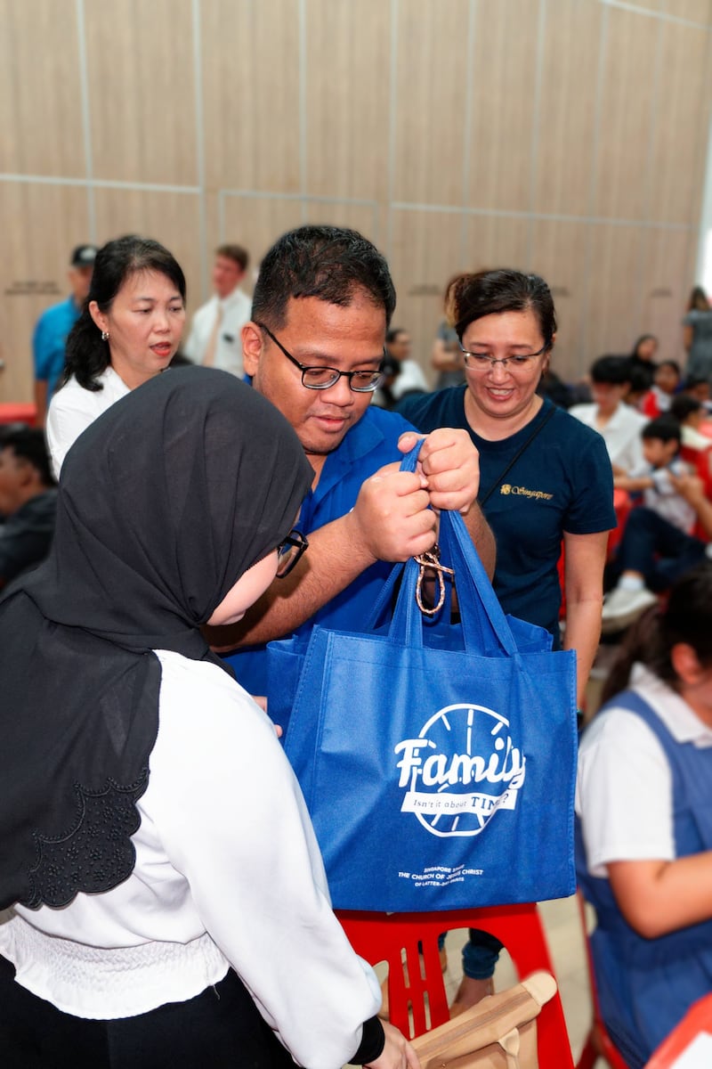 Membros de A Igreja de Jesus Cristo dos Santos dos Últimos Dias e voluntários da Fundação Rahmatan Lil Alamin entregam sacolas de rações secas doadas a um destinatário no projeto de serviço Estudo Awards no Centro Comunitário West Coast em Singapura, 6 de dezembro de 2025.